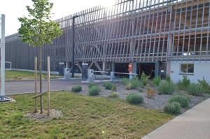 Façade en bois moderne et accès au parking EFFIA Valmy à Dijon : voies d'entrée sécurisées avec barrières automatiques, bornes de ticket et aménagement paysager soigné à proximité.