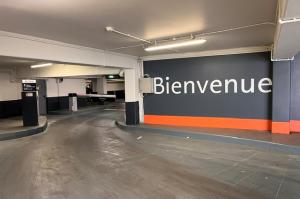 Voie d'accès couverte du parking avec borne d'entrée, barrière automatique et mur d'accueil signalétique.