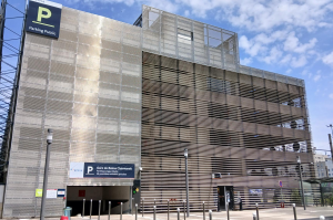 Façade du parking couvert avec accès véhicule et enseignes d'information à l'entrée.