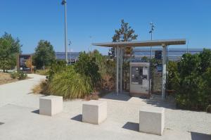 Caisse automatique EFFIA sous un abri vitré, bordée de blocs de béton et de végétation sur le parking.