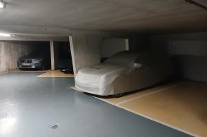 Voiture sous bâche blanche et Volvo grise garées dans un parking souterrain.