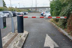 Voie d'accès au parking extérieur avec barrière automatique et borne de contrôle.