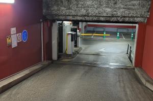 Rampe d'accès intérieure bordée de murs rouges menant aux bornes et barrières du parking.