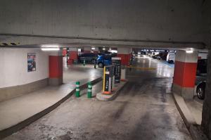 Rampe d'accès intérieure menant à une borne de contrôle et à une barrière automatique dans un parking couvert.