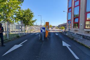 Voies d'accès et de sortie du parking équipées d'une borne orange et d'une barrière automatique.