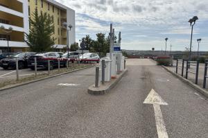 Point de contrôle du parking avec bornes de distribution de tickets et barrières levantes devant les bâtiments hospitaliers.