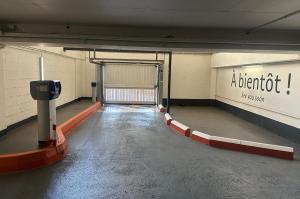 Voie de sortie de parking souterrain avec borne de validation du ticket, portail basculant et inscription « À bientôt ! » sur le mur.