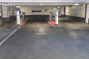 Double voie d'accès intérieure avec bornes de distribution de tickets et barrières levantes sous le panneau « Bienvenue ».