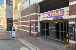 Entrée du Parc Relais Les Arts avec grille automatique, enseigne lumineuse violette et totem d'information des horaires et tarifs.