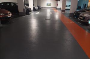 Allée de circulation intérieure d'un parking couvert bordée de voitures.