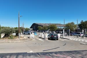 Voies d'accès d'un parking de gare avec barrières de contrôle et véhicules engagés.