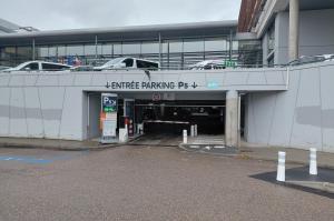 Entrée du parking P5 en sous-sol avec barrière automatique et signalétique.Voie de sortie du parking P5 sous un bâtiment avec une barrière de contrôle.