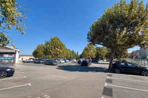 Grand parking extérieur arboré avec de nombreuses places de stationnement.
