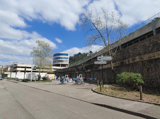 Vue d'ensemble du parking EFFIA Gare de Vienne : barrières, panneau d'accueil et bâtiments au loin.