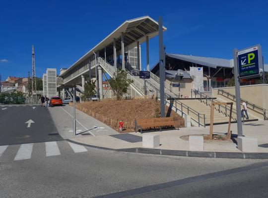 aménagement moderne des abords de la Gare de Béziers avec la nouvelle passerelle piétonne et le jalonnement dynamique du parking EFFIA : l'image montre un espace public optimisé incluant des zones piétonnes, du mobilier urbain et une signalétique indiquant le nombre de places disponibles en temps réel.