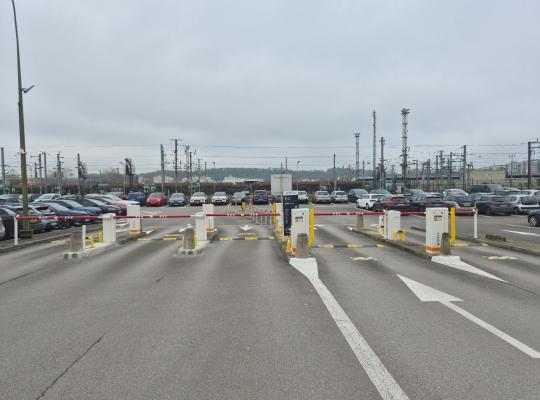 vue large des voies d'entrée d'un grand parking EFFIA à ciel ouvert: plusieurs couloirs d'accès avec barrières automatiques permettent de gérer un flux important de voitures, avec les infrastructures ferroviaires visibles en arrière-plan.