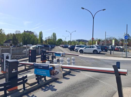vue d'ensemble d'un parking extérieur EFFIA sécurisé par des bornes et une signalétique claire: l'espace de stationnement est situé à proximité de voies ferrées, idéal pour les usagers du train cherchant une solution de parking pratique.