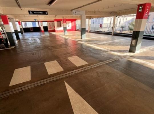 Vue intérieure du niveau 2 du parking couvert EFFIA Diderot : un espace de stationnement lumineux et propre, doté d'un marquage au sol clair, de flèches de circulation et d'une signalétique dédiée pour les places PMR.