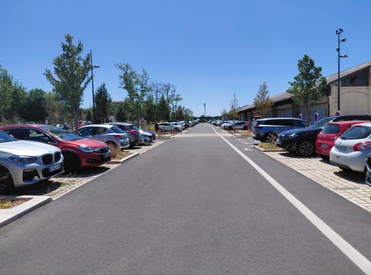 Zone de contrôle d'accès du parking extérieur EFFIA : l'image montre les barrières automatiques, les bornes de ticket, les totems de signalétique tarifaire ainsi qu'un bâtiment d'accueil moderne au revêtement en bois.