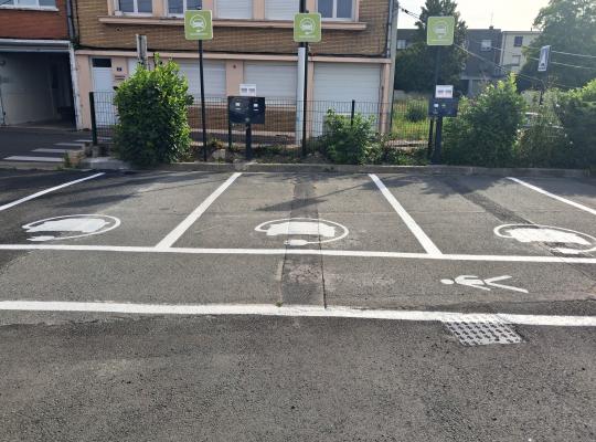 Trois places de parking IRVE signalées par des logos et des panneaux verts.