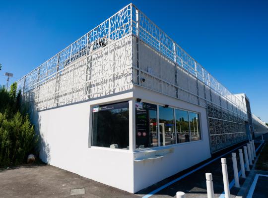 Bâtiment d'accueil du parking EFFIA Gare d'Esbly : une architecture moderne habillée d'une résille métallique blanche tressée sous un ciel bleu.