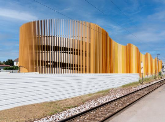 Façade architecturale moderne du parking EFFIA de la gare de Cormeilles-en-Parisis : une structure vêtue de lames verticales aux nuances dorées, idéalement située le long des voies ferrées.