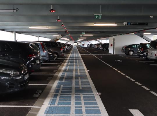 Intérieur du Parking Relais La Verrière (EFFIA) : allée de circulation avec cheminement piéton bleu, guidage à la place par voyants lumineux et places réservées.