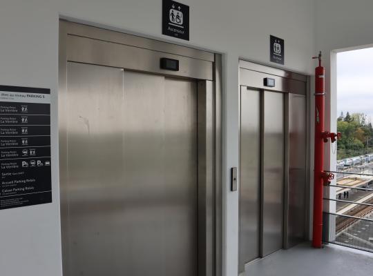 Ascenseurs modernisés au Niveau 5 du Parking Relais La Verrière (EFFIA) avec vue panoramique sur la gare et panneau d'orientation clair des étages.