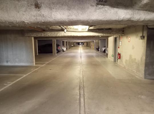 Allée centrale éclairée et emplacements numérotés d'un parking souterrain bétonné et sécurisé.