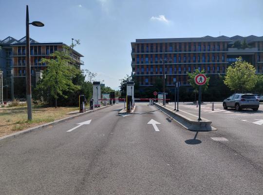 Bornes d'accès et barrières automatiques à l'entrée du parking devant les bâtiments du site.