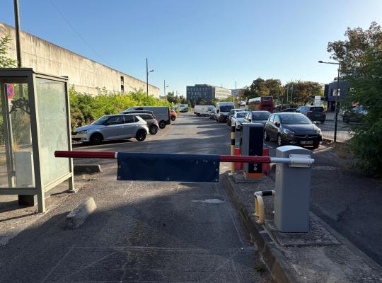 Barrière de sortie EFFIA fermée et borne de paiement devant un parking extérieur.