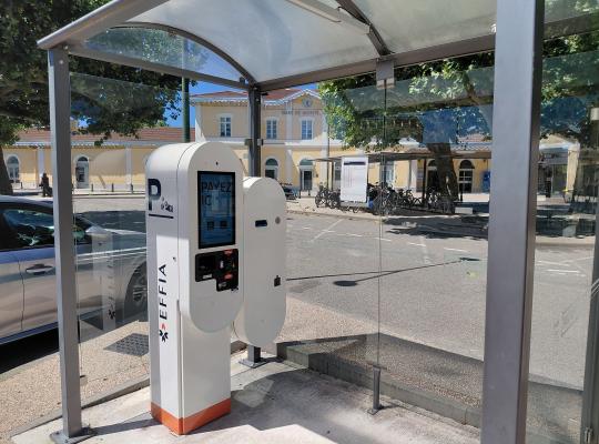 Caisse automatique de paiement installée sous abri vitré, face au bâtiment de la gare.