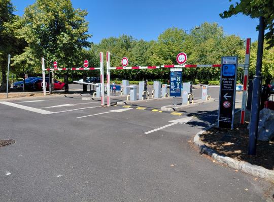 Voies d'accès et de sortie du parking relais équipées de barrières automatiques et du panneau d'information tarifaire.