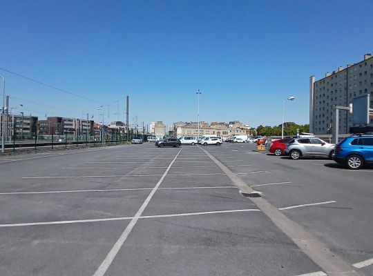 Aire de stationnement extérieure asphaltée avec emplacements délimités le long des voies ferrées.