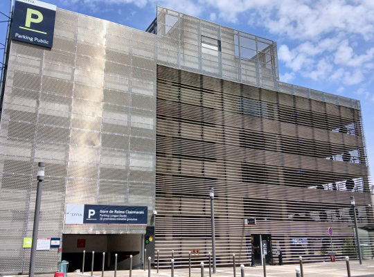 Façade du parking couvert avec accès véhicule et enseignes d'information à l'entrée.