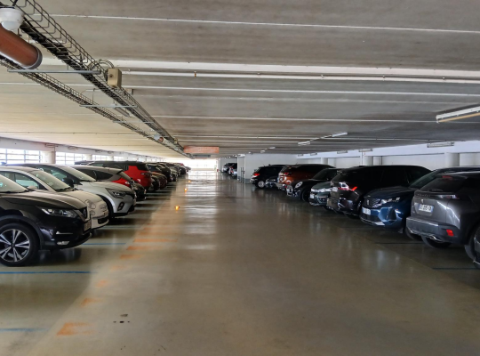 Niveau de stationnement couvert et éclairé avec rangées de véhicules garés.