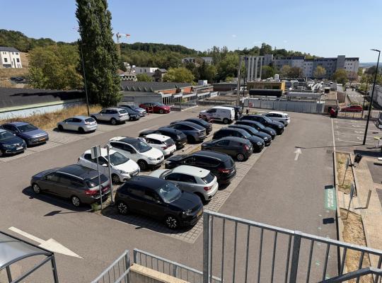 Vue en hauteur d'un parking extérieur asphalté rempli de voitures stationnées.