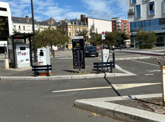 Accès au parking avec totem tarifaire, borne d'entrée à barrière et caisse automatique couverte.
