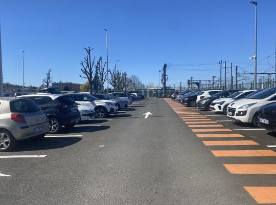 Allée de circulation bordée de voitures garées et passage piéton orange.