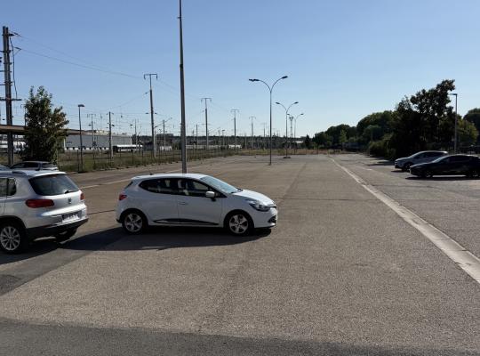 Parking extérieur à ciel ouvert longeant les voies ferrées avec emplacements de stationnement.