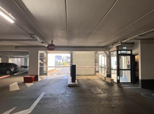 Voie de sortie du parking couvert avec barrières automatiques, porte sectionnelle et accès piéton vitré.