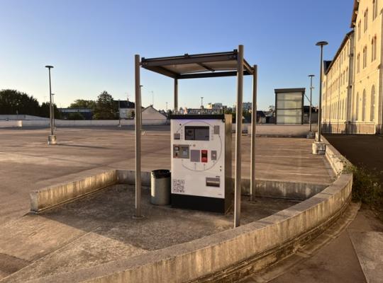 Borne de paiement automatique installée sous un abri couvert sur la terrasse du parking.
