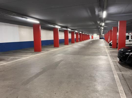 Allee de circulation couverte et places de stationnement délimitées au sol, bordées de poteaux rouges.