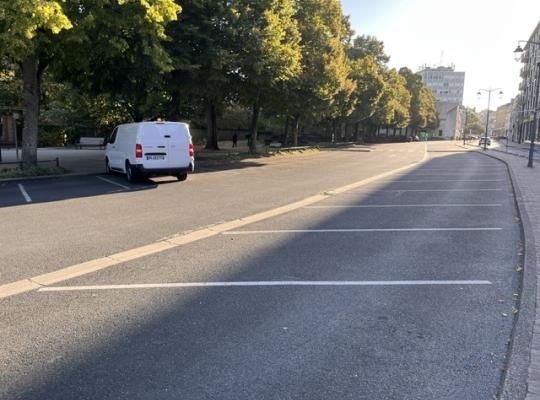 Emplacements de stationnement extérieurs aménagés en épi le long d'une allée arborée.