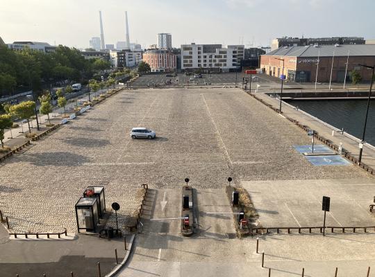 Vue panoramique en hauteur de l'aire de stationnement pavée bordant le bassin, avec ses voies d'accès et ses équipements.