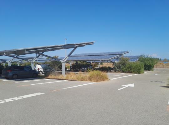 Places de stationnement abritées par de grandes structures d'ombrières photovoltaïques en extérieur.