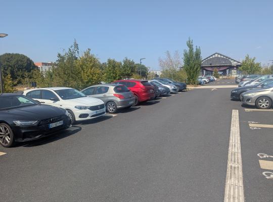 Rangées de stationnement en extérieur bordant une allée bitumée avec voitures garées.
