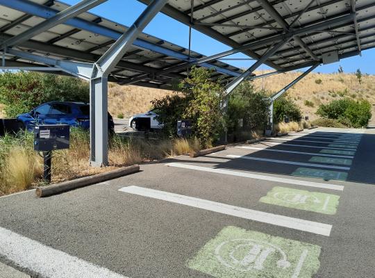 Emplacements dédiés à la recharge des véhicules électriques avec marquages verts au sol et bornes sous ombrière.