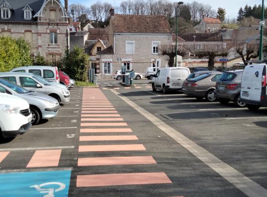 Allée centrale du parking EFFIA avec places de stationnement, cheminement piéton balisé et emplacement PMR.