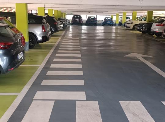 Emplacements de stationnement et allée de circulation dans un parking couvert.